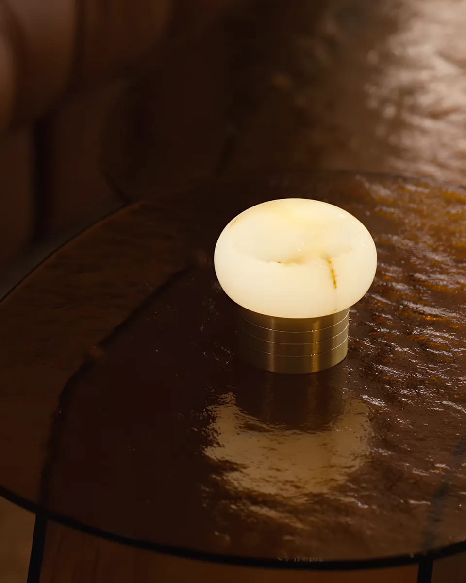 An alabaster lamp glowing on a smoked-glass table beside a leather lounge